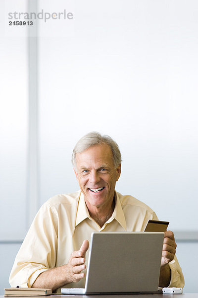 Mann beim Online-Einkauf mit Kreditkarte  lächelnd vor der Kamera
