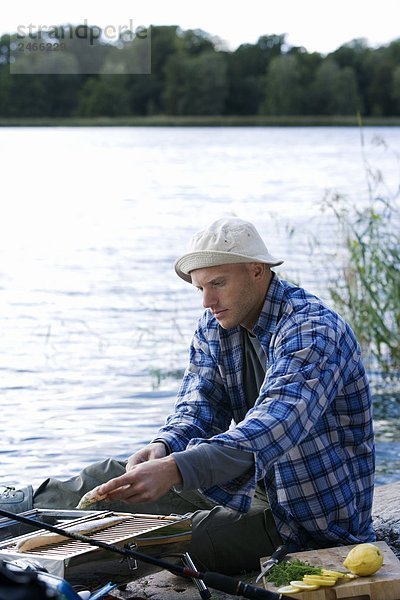 Ein Mann Grillen Fisch am Wasser Schweden.