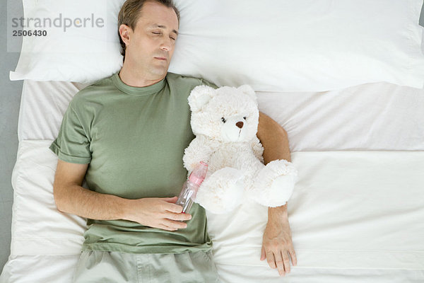 Vater schläft im Bett  hält Babyflasche und Teddybär  Draufsicht