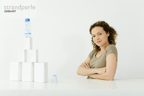 Frau neben gestapelten Milchkartons und Babyflasche  Arme gefaltet  Kamera lächelnd