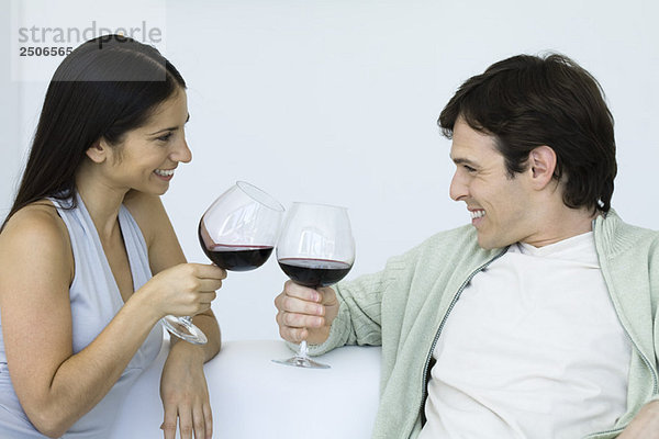 Paar auf der Couch sitzend  klirrende Weingläser  einander anlächelnd