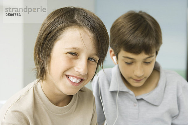 Jungen teilen sich Kopfhörer  einer lächelt in die Kamera  der andere schaut nach unten.