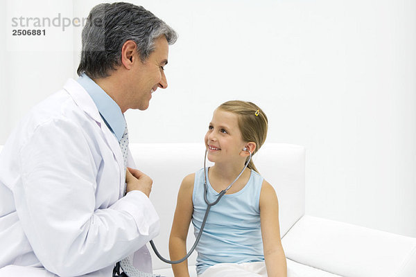 Mädchen hört Arztherz mit Stethoskop  lächelnd