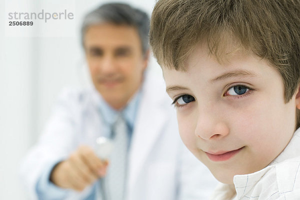 Junge lächelt in die Kamera  Arzt hält Stethoskop im Hintergrund