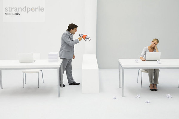 Vorgesetzter schreit Mitarbeiter mit Megaphon an  Frau sitzt mit Laptop  umgeben von zerknittertem Papier