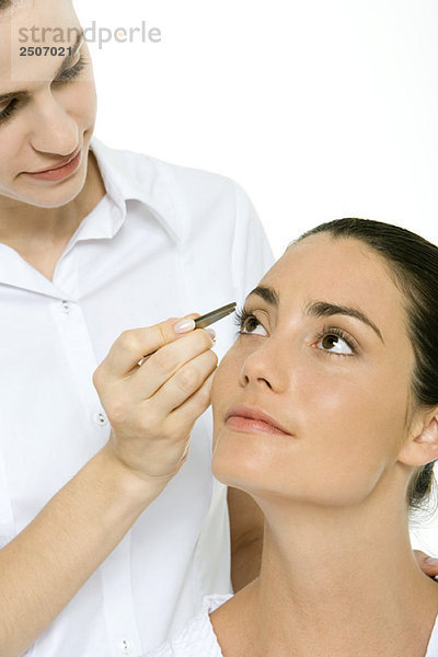 Frau schaut auf  Kosmetikerin benutzt eine Pinzette  um eine Wimper zu entfernen.