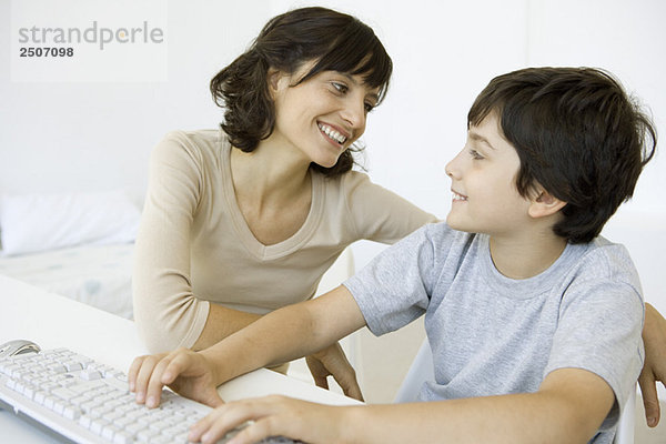 Mutter und Sohn sitzen und lächeln sich an  Junge mit Tastatur
