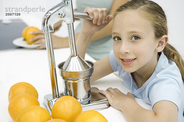 Kleines Mädchen macht frischen Orangensaft mit Zitruspresse  Mutter im Hintergrund