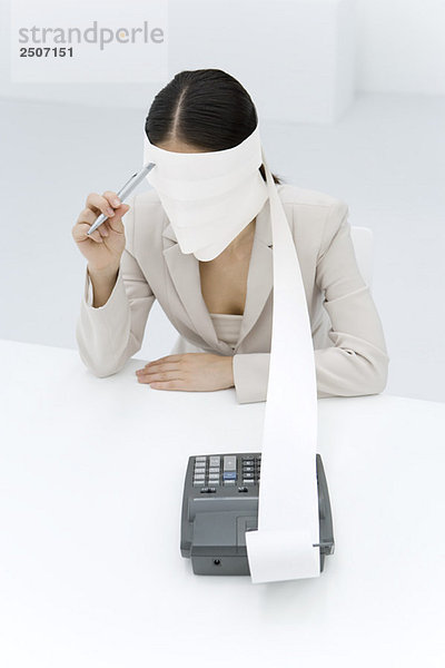 Frau sitzend mit um den Kopf gewickeltem Maschinenband  Stift an der Stirn haltend