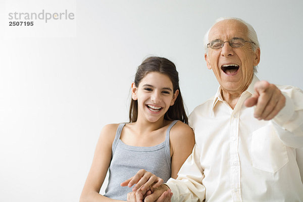 Teenagermädchen Seite an Seite mit Großvater  beide lachend  älterer Mann auf Kamera zeigend