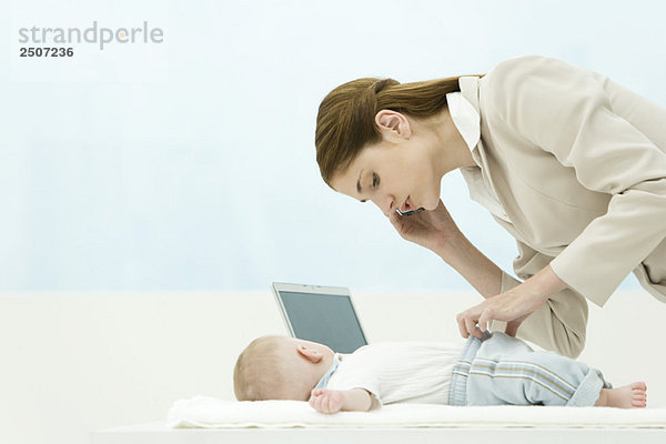 Professionelle Frau im Büro  mit dem Handy  Bücken über Baby auf dem Schreibtisch