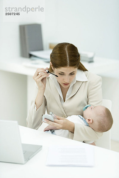 Professionelle Frau im Büro  Wimperntusche auftragend  schlafendes Baby haltend