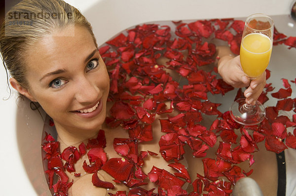 Junge Frau entspannt in einer Badewanne mit Rosenblättern  lächelnd  Portrait