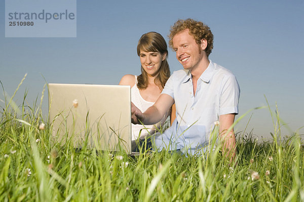 Deutschland  Bayern  Junges Paar auf der Wiese  mit Laptop  Portrait