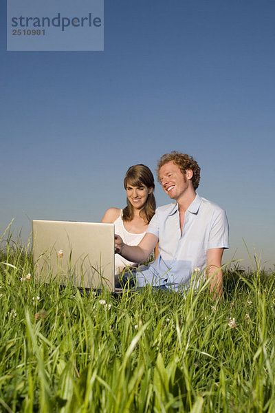 Deutschland  Bayern  Junges Paar auf der Wiese  mit Laptop  Portrait