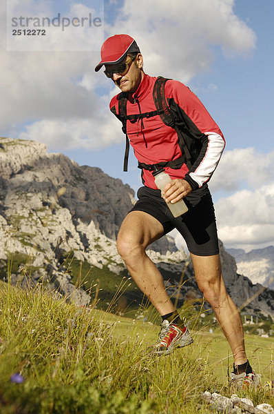 Männlich Athlet in Sportswear die grasbewachsenen Hügel in Trentino  Südtirol  im Hintergrund laufen die Dolomiten