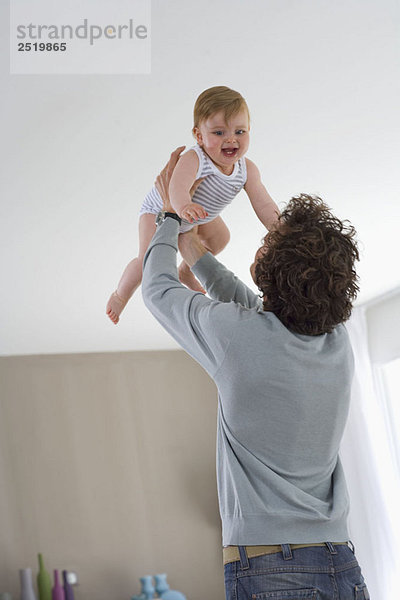 Vater hält glückliches Baby in der Luft im Haus