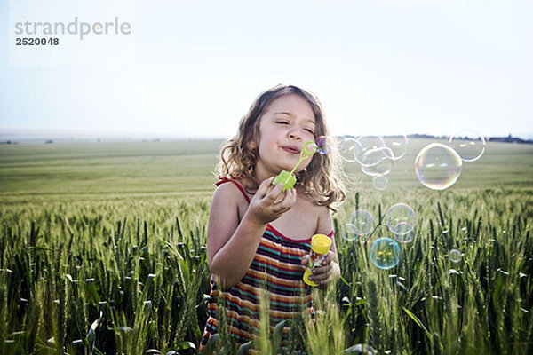 Mädchen bläst Blasen im Weizenfeld