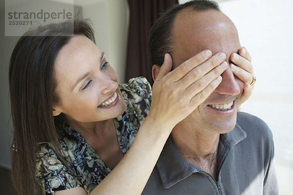 Frau versteckt die Augen ihres Mannes  lächelnd