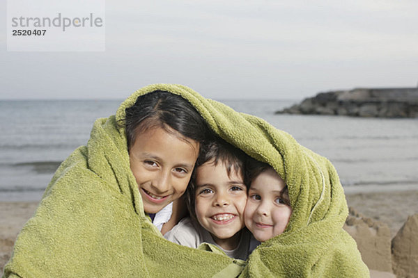 Drei kleine Kinder im Handtuch am Strand