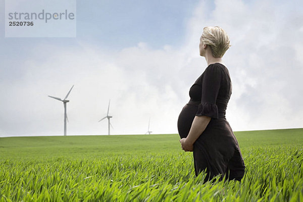 Schwangere Frau schaut auf Windkraftanlagen