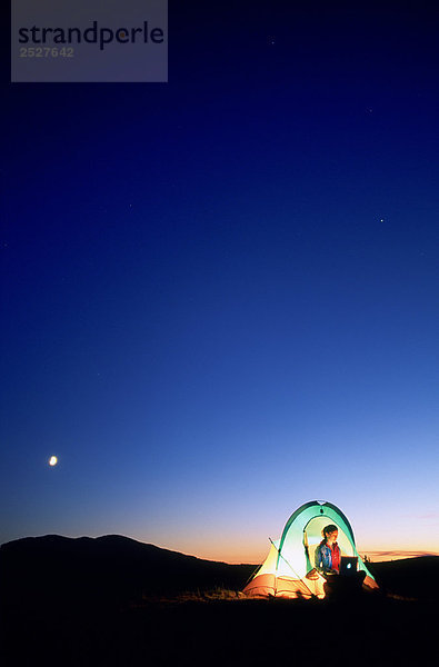 Frau im Zelt in der Nacht mit Laptop  British Columbia.