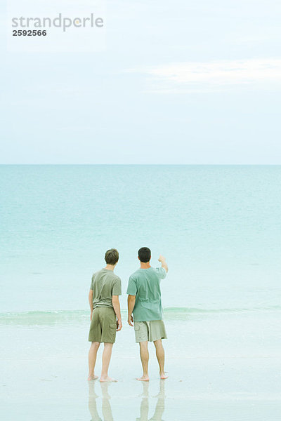 Zwei Männer  die am Strand stehen und den Horizont betrachten.