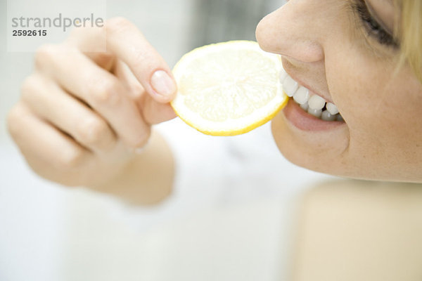 Frau beißt in Zitronenscheibe  lächelnd  Nahaufnahme