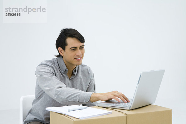 Mann  der am Schreibtisch sitzt und einen Laptop benutzt.