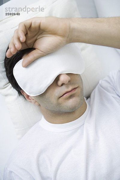 Mann liegend mit Augenmaske  Hand auf Kopf