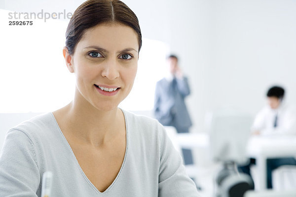 Professionelle Frau lächelt vor der Kamera  männliche Kollegen im Hintergrund