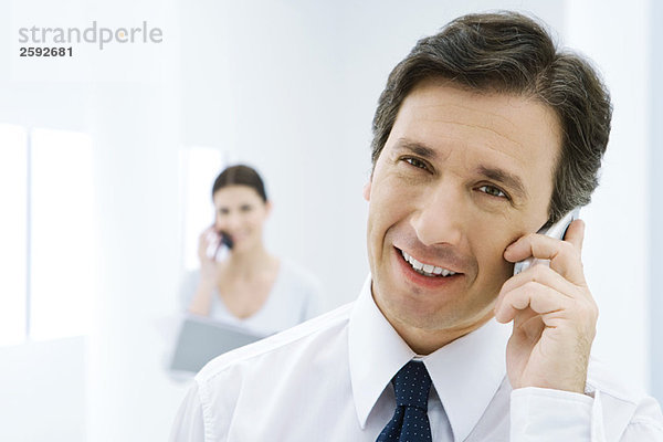 Professioneller Mann mit Handy  lächelnd in die Kamera  Frau am Telefon im Hintergrund
