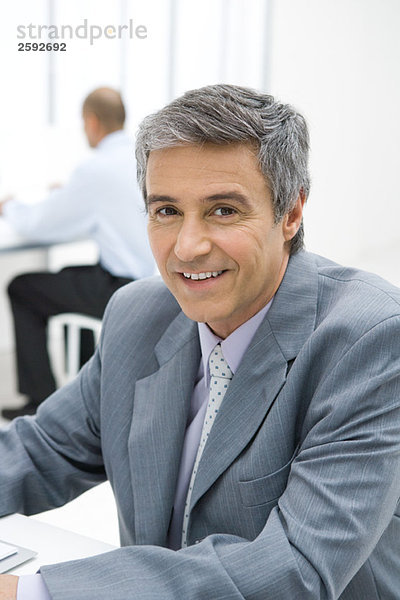 Geschäftsmann im Büro sitzend  lächelnd vor der Kamera  Porträt