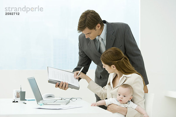 Professionelle Frau unterzeichnet Dokument im Büro  hält Baby auf Schoß