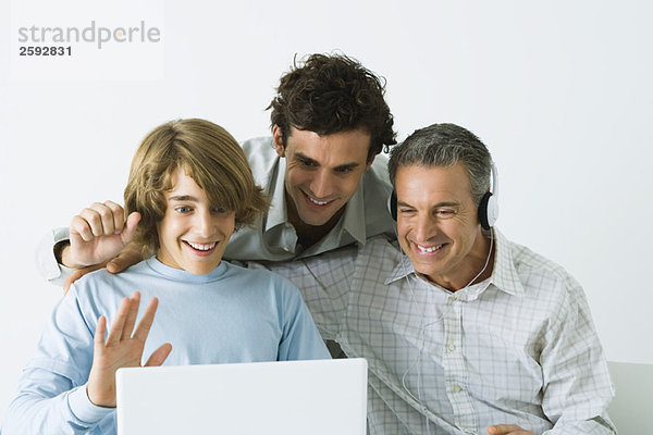 Vater und zwei Söhne schauen gemeinsam auf den Laptop  Vater trägt Kopfhörer