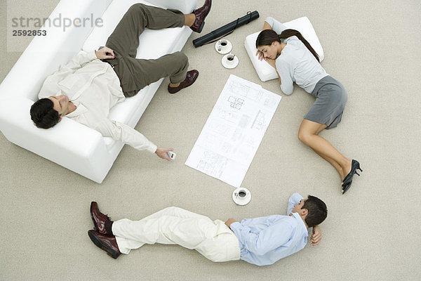 Team von Profis  die auf dem Boden und Sofa schlafen  Blaupause auf dem Boden zwischen ihnen  Blick nach oben