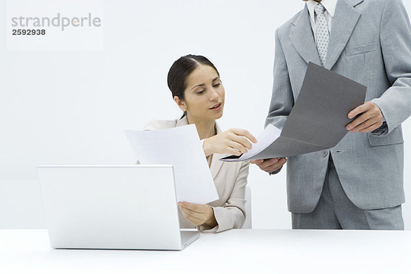 Geschäftsfrau sitzt am Schreibtisch und bespricht das Dokument mit einem männlichen Kollegen.