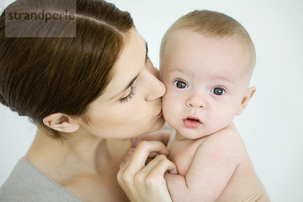 Mutter küsst Kleinkind auf die Wange  Baby schaut in die Kamera