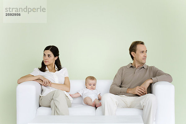 Paar auf der Couch sitzend mit Baby zwischen ihnen  beide schauen weg