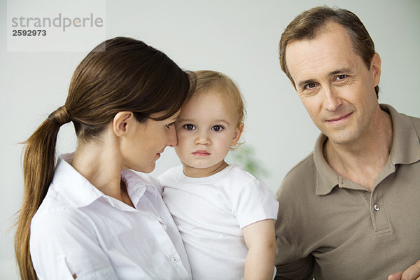 Mann neben Frau und Kleinkind  lächelnd vor der Kamera