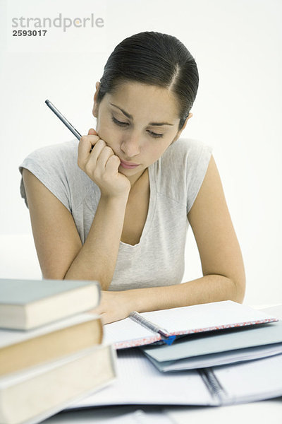 Junge Frau sitzt mit Bücherstapel  studiert Notizbuch