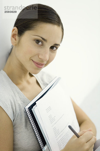 Junge Frau mit Dokumenten und Notizbuch  lächelnd vor der Kamera