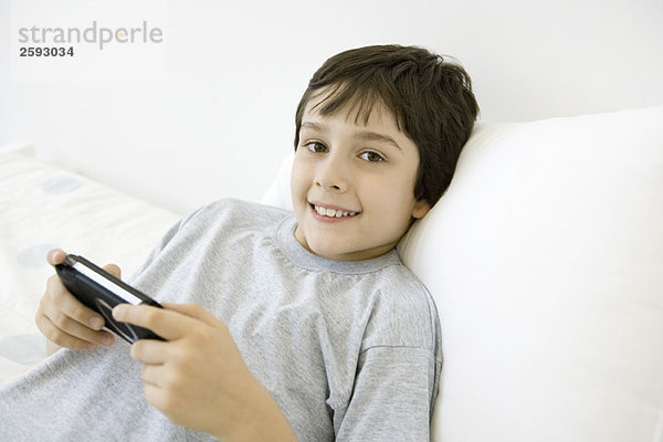 Junge liegend  Handheld-Videospiel spielend  Kamera lächelnd