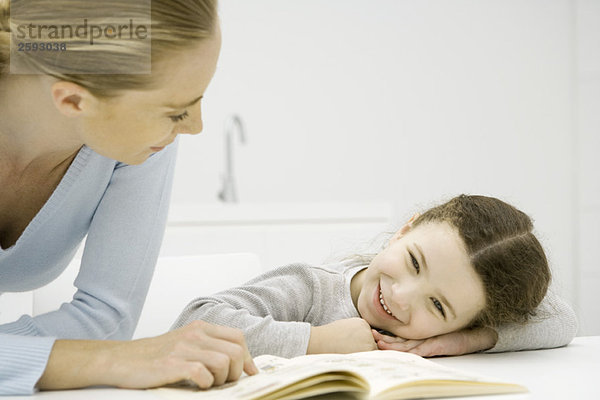 Mutter und Tochter schauen gemeinsam auf das Buch  Mädchen ruht mit dem Kopf auf den Armen