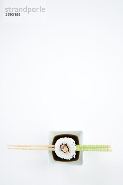 Einzelstück Maki-Sushi auf Essstäbchen über Sojasauce  Draufsicht