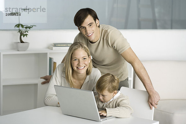 Familie versammelt um Laptop-Computer  kleiner Junge beim Tippen  Eltern lächeln vor der Kamera