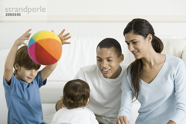 Familie versammelt um Kleinkind Mädchen  lächelnd  Junge wirft Ball in die Luft