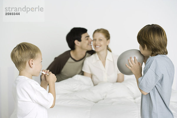 Zwei Jungen  die Luftballons aufblasen  Eltern lächeln auf dem Bett im Hintergrund