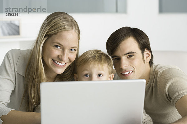 Eltern und junger Sohn mit Laptop-Computer  lächelnd vor der Kamera