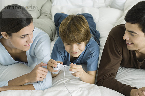 Familie liegt zusammen auf dem Bett  Junge spielt Videospiel